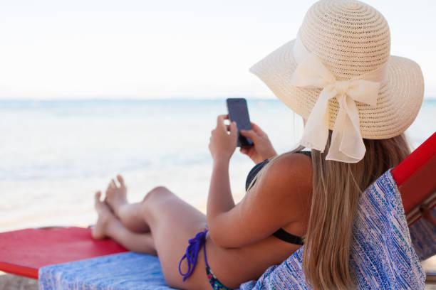 istock Young beautiful woman with sun hat on deck chair using phone on the beach 1781961611