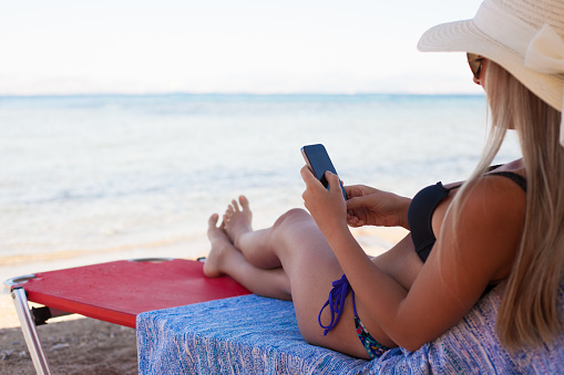 Beautiful woman relaxing and using smart phone on a beach