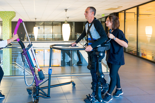 Mechanical exoskeleton. Female physiotherapy doctor helping disabled person with robotic skeleton to walk. Futuristic rehabilitation, Physiotherapy in a modern hospital