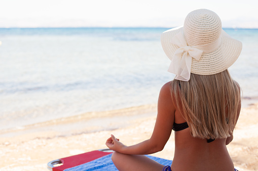 Back view of a woman with sun hat relaxing on a deck chair at the beach.