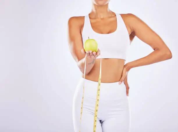 Photo of Health, apple and tape measure for diet of woman in studio for healthy lifestyle, weight loss or fitness. Female on a white background for health, wellness and fruit motivation for healthcare goals