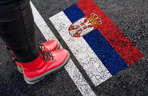 a woman with a boots standing on asphalt next to flag of Serbia and border