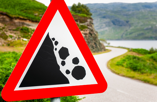 A rock fall danger warning sign on a winding country road in the Scottish Highlands.