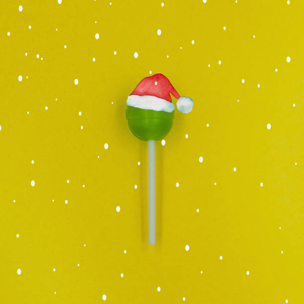 bastoncino di zucchero verde che indossa un cappello di babbo natale su uno sfondo giallo con neve che cade. - falling candy christmas candy cane foto e immagini stock