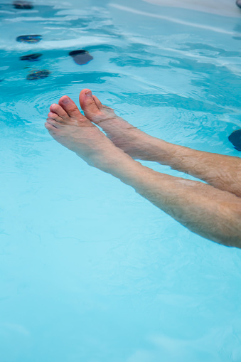 Anonymous man relaxing and floating in a swim hot tub focus on legs relaxing in the tub