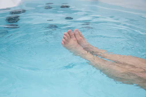 Anonymous man relaxing and floating in a swim hot tub focus on legs relaxing in the tub