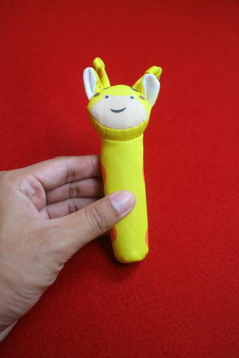 A hand holding yellow giraffe shaped baby holding toy that makes a sound when squeezed. on a red background