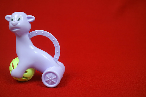 A toy shaped like an alpaca animal, purple in color, holding a ball. on a red background