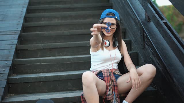 Young Woman Playing With Fidget Spinner Sitting On The Steps Outdoors