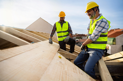 Two mid-adult male Caucasian roofers, working on a rooftop, while making a roof beam