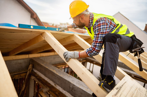 Mid-adult male Caucasian roofer, using level while working on a roof beam at the construction site