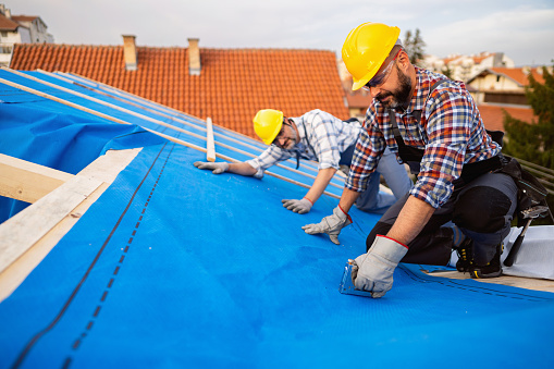 Two mid-adult male Caucasian roofers, placing an vapor permeable foil for an roof hydro isolation