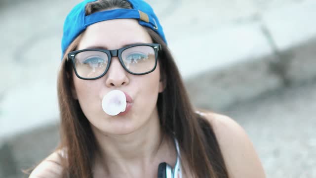 Young Woman Chewing Gum And Blowing Bubbles Outdoors