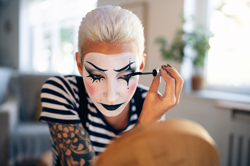 Young woman, a mime artist, applying face paint while getting ready for pantomime show.