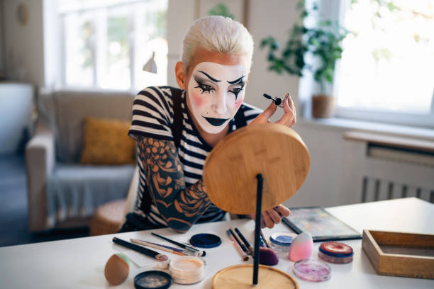 Young woman, a mime artist, applying face paint while getting ready for pantomime show.