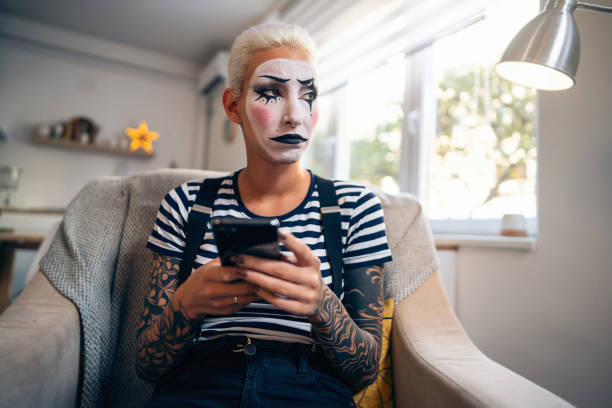 giovane donna triste, un'artista mima, che invia messaggi di testo sul suo telefono mentre si prepara per lo spettacolo di pantomima. - clown mime sadness depression foto e immagini stock