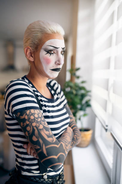 不幸な若い女性、パントマイムアーティストが腕を組んで窓辺に立っている肖像画。 - clown mime sadness depression ストックフォトと画像