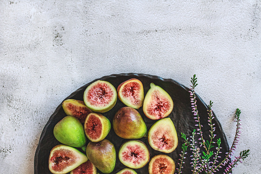 Still life with ripe sliced and whole fresh figs as healthy food for holidays. Black lava stone plate on gray concrete background and Lavender as decoration. Rustic background. Copy space. Flat lay. Overhead view.