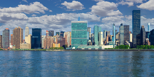 A wooden dock in the East River with a cityscape of the New York in the background, with clouds on a blue sky