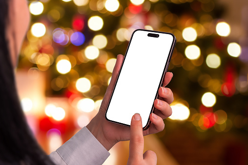 Woman using phone mockup near a sparkling Christmas tree with bokeh lights