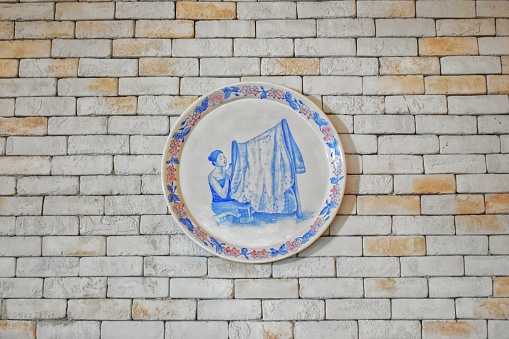 art of a woman making batik cloth on a plate attached to a white brick wall