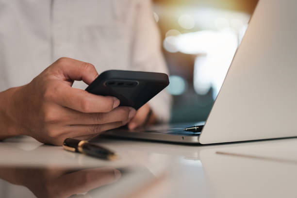 istock Businessman hand holding mobile smartphone on a table with a laptop at office.. 1782108872