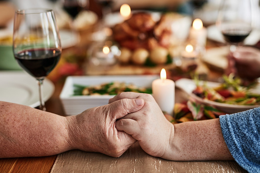 Thanksgiving, holding hands and praying on table, closeup or home for dinner, festive holiday or vegetables. Christmas lunch party, event or people with faith, meat or chicken with gratitude in house