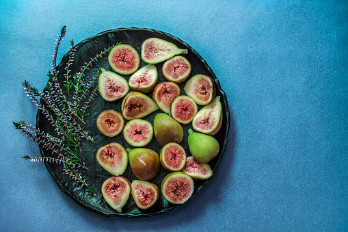Still life with ripe sliced and whole fresh figs as healthy food for holidays. Black lava stone plate on blue concrete background and Lavender as decoration. Rustic background. Copy space. Flat lay. Overhead view.
