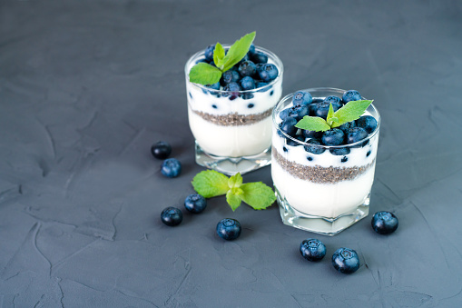 Layered light and healthy dessert with freshly picked blueberries, yogurt and chia seeds on the dark background. Diet breakfast. ?lose-up. Place for text.