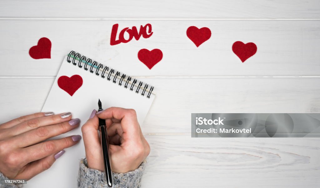 Woman's hands write a love letter on notepad. Romantic greeting for Valentine's Day. Valentine's Day holiday concept. Top view. Flatlay. Copy space. Above Stock Photo