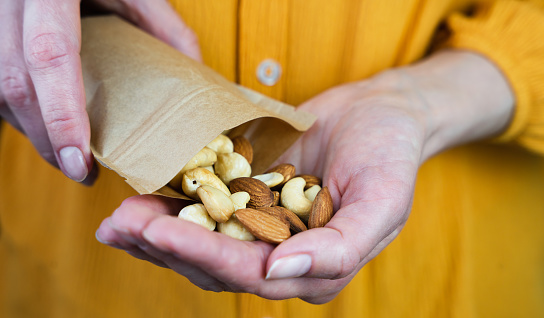 The girl pours a mix of nuts from a paper bag into her hand. Healthy breakfast. Healthy food concept. Close-up. Selective focus.