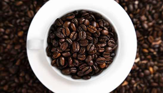 Coffee beans in a white cup on a coffee background. Banner. Top view. Close-up. Selective focus.