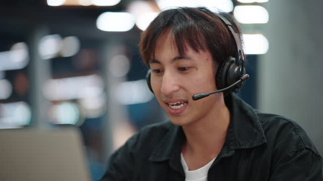 Asian man call center agent answering calls and wearing a headset at work.