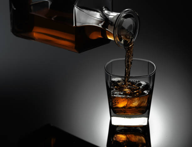 whiskey wird aus einem dekanter in ein gefrorenes glas mit natürlichem eis gegossen. - wine decanter elegance pouring stock-fotos und bilder