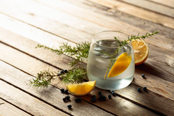 istock Alcohol drink (gin tonic cocktail) with lemon, juniper branch, and ice on rustic wooden table. 1782164238