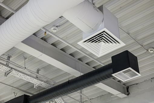 Two ventilation duct systems with grilles suspended under ceiling in commercial building. Supply and exhaust