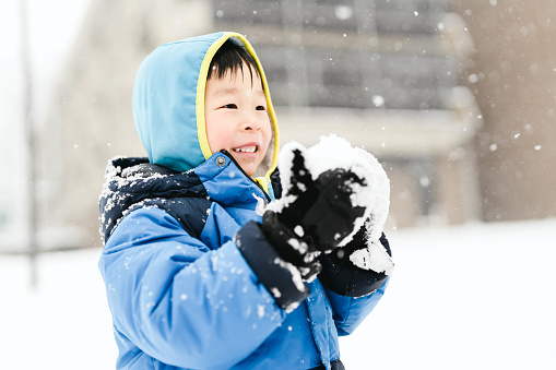 Cute little boy having fun and playing outdoors during snowfall