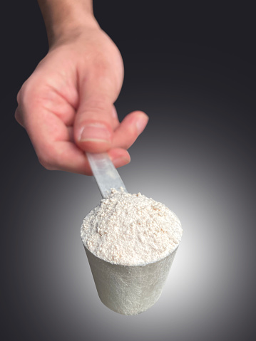 Hand holding whey protein powder in measuring plastic spoon with clipping path