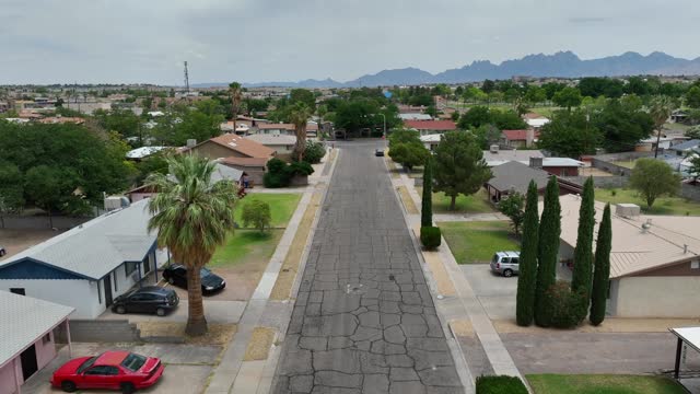 American neighborhood in the Southwest. Aerial reverse dolly shot over street lined by houses and homes.