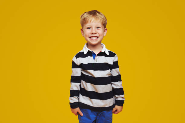 istock Cheerful positive boy with blonde hair smiling for camera while standing against yellow background. 1782201543
