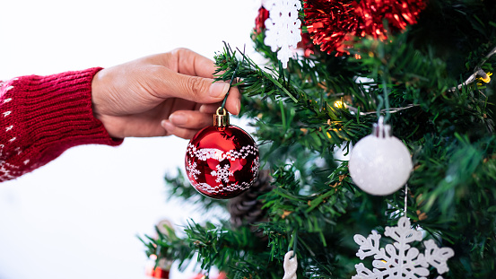 Woman decorating christmas tree with red balls in living room house. Merry christmas and happy new year concept. Girl putting Xmas ornaments on spruce branches. Family cozy moments