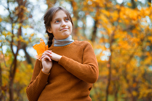a young teenage girl poses in an autumn forest, enjoying the beautiful nature and bright yellow leaves
