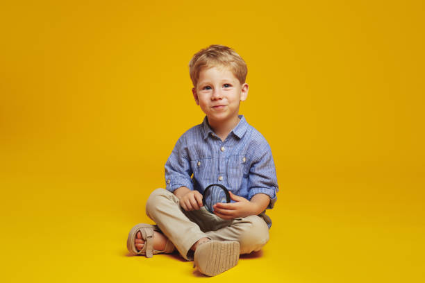 istock Curious cute boy holding magnifier and looking at camera while sitting on floor with crossed legs 1782204233