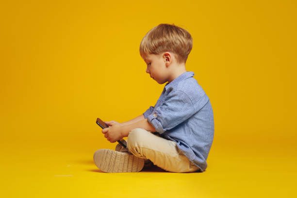 istock Addicted little boy sitting on floor with crossed legs while playing video game on mobile phone. 1782208474