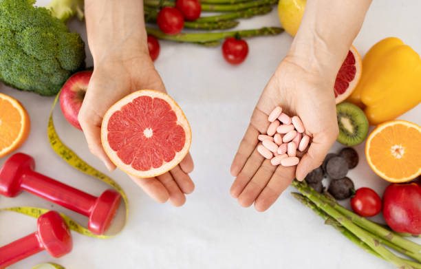 成熟した白人の栄養士は、有機野菜、果物、ダンベルと一緒にテーブルでグレープフルーツとビタミンの丸薬を保持します - nutritional supplement pill eating food ストックフォトと画像