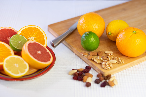 Close-up of a mix of citrus fruits, whole or cut in half. Oranges, grapefruits, lemons and limes on a wooden cutting board with dried fruit. Healthy eating concept