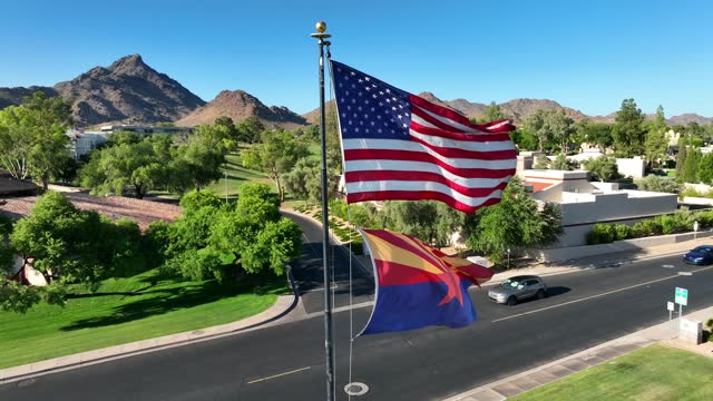 American and Arizona flags waving in luxurious country club neighborhood. Aerial establishing shot on bright afternoon.