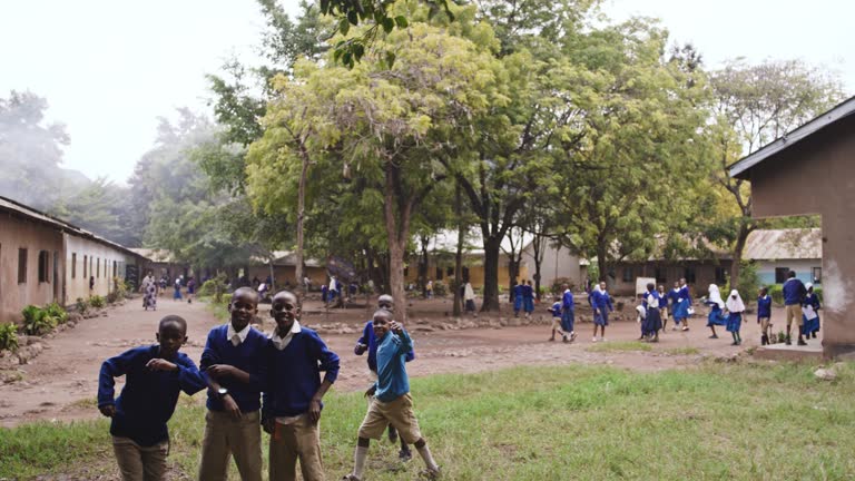 Slow motion shot of playful schoolboys in uniforms,greeting and looking at the cameral. Children are playing together in playground. School in rural area.
