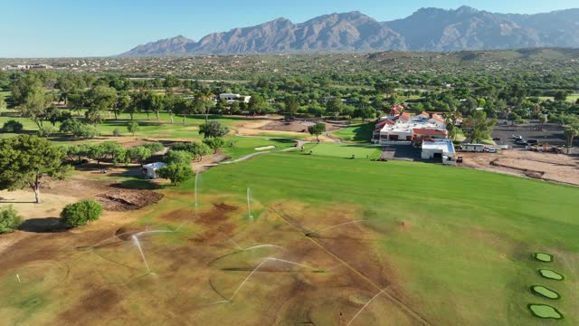 Brown golf course being watered by irrigation system in hot and dry desert. Aerial establishing shot of country clubs in Southwest USA.