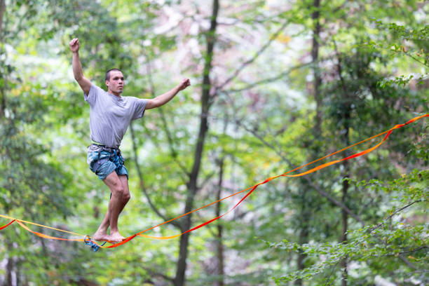 A young guy walks on a highline in a beautiful green forrest.